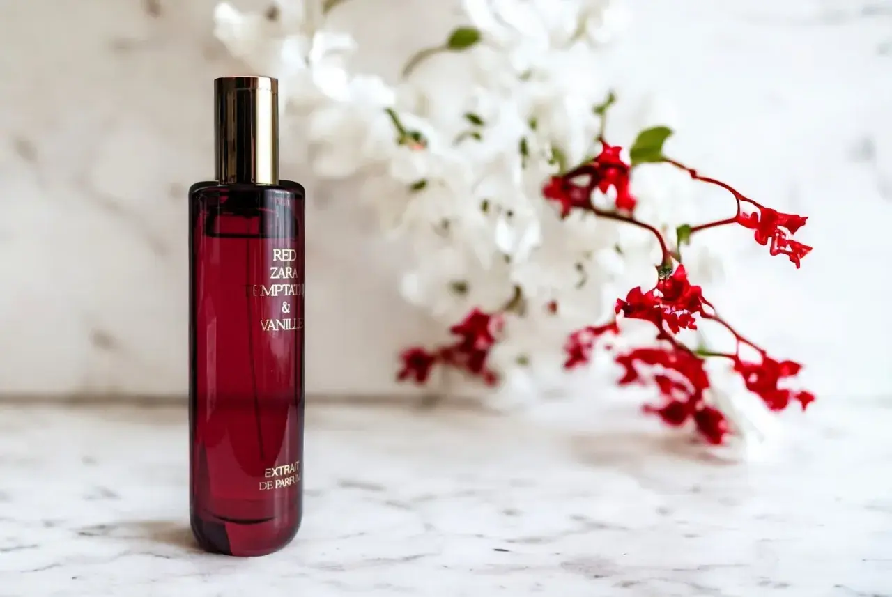 Czerwona butelka perfum Red Zara Temptation & Vanilla, z kwiatami w tle. Idealny odpowiednik dla miłośniczek słodkich, zmysłowych zapachów.