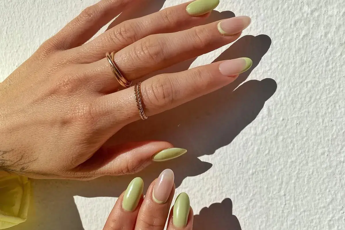 Delikatny manicure naturalny z pastelowo-zielonym akcentem na końcówkach. Dłonie ozdobione złotymi pierścionkami.