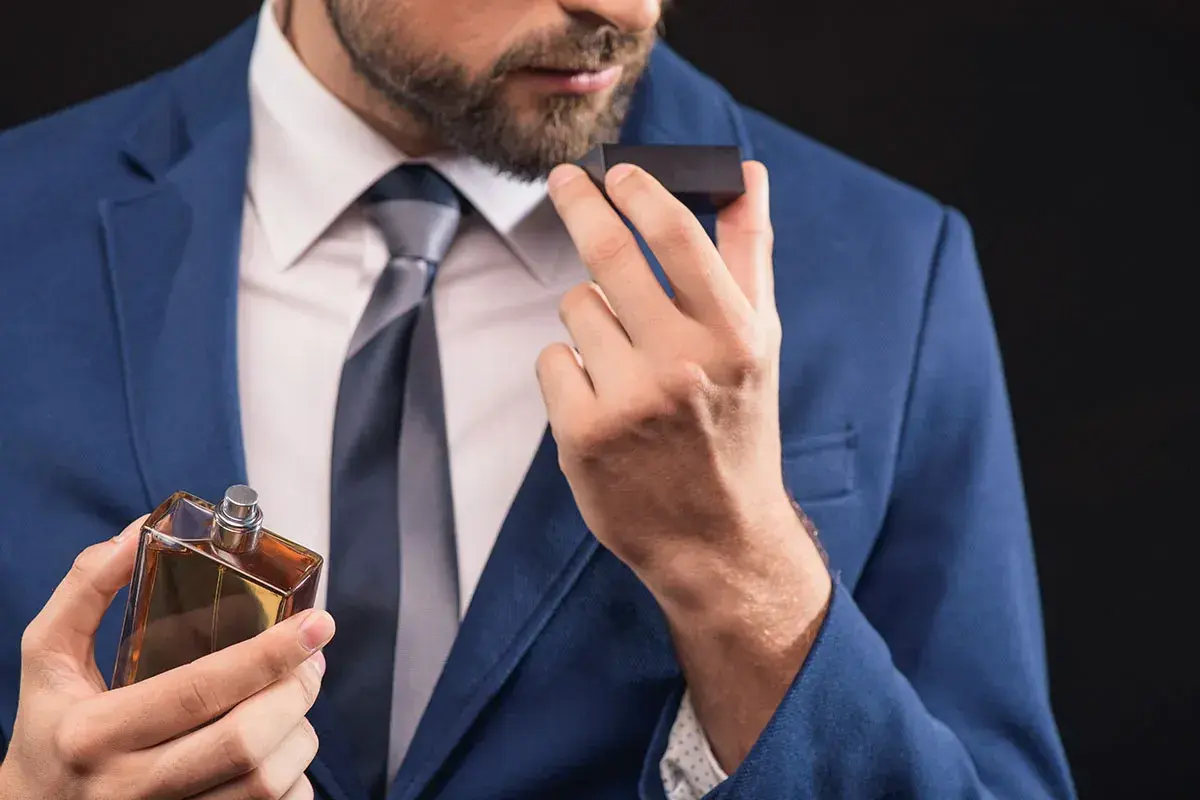Elegancki mężczyzna w niebieskiej marynarce wącha perfumy. Zapach, niczym karnozyna, dodaje mu pewności siebie.