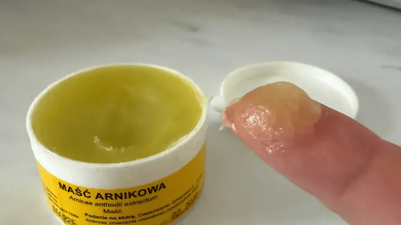 Maść z arniki na twarz, w żółtym słoiczku, z odrobiną na palcu. Idealna do pielęgnacji skóry.
