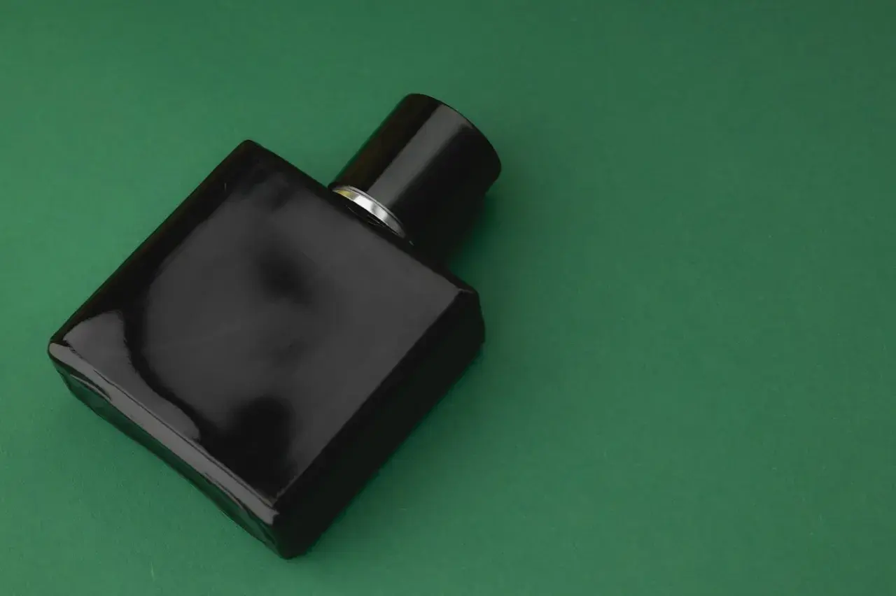 Elegancka, czarna butelka perfum z nutami **vetiver** na zielonym tle.