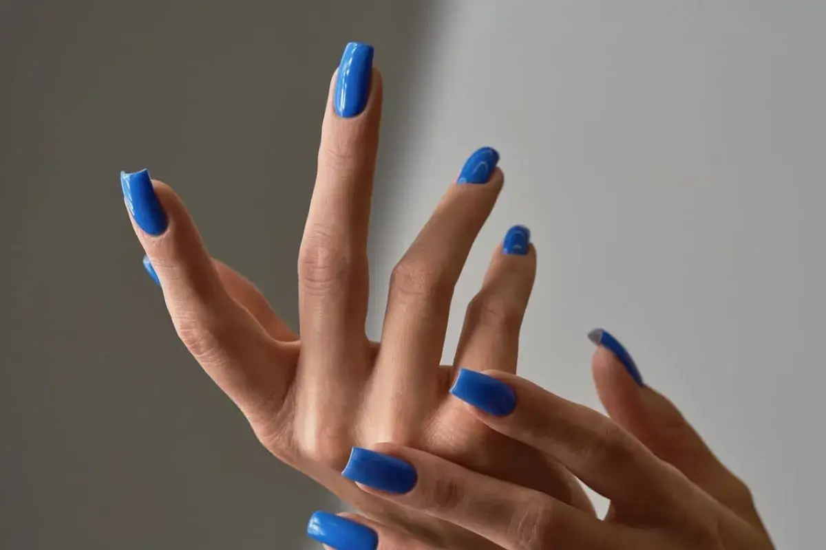 Dłonie z idealnym, letnim manicure w odcieniu kobaltowego błękitu. Paznokcie są długie, kwadratowe i błyszczące.