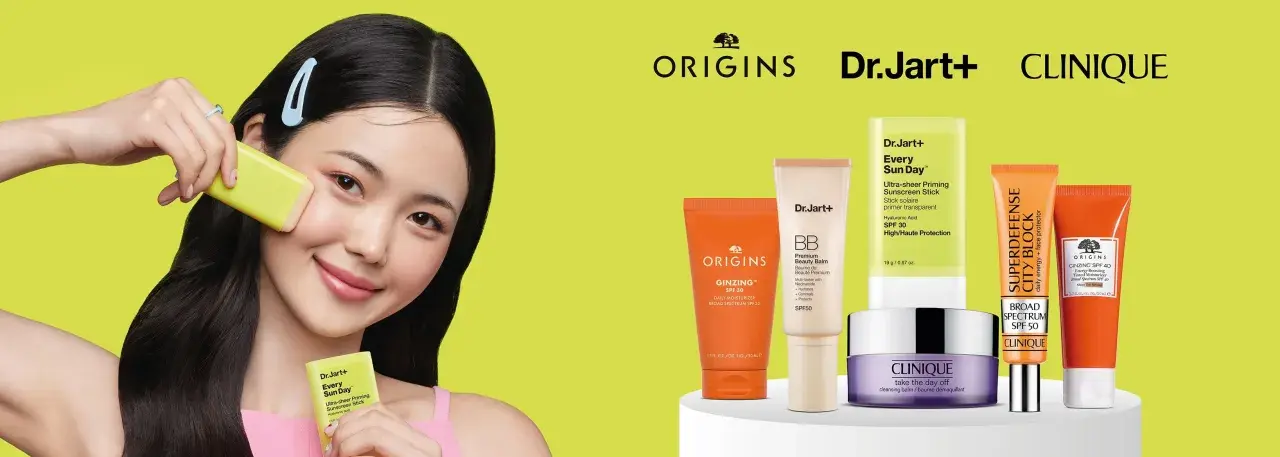 Młoda kobieta aplikuje na twarz kosmetyk z filtrem SPF. Obok niej produkty Origins, Dr.Jart+ i Clinique, pomagające wybrać jaki SPF do twarzy będzie najlepszy.