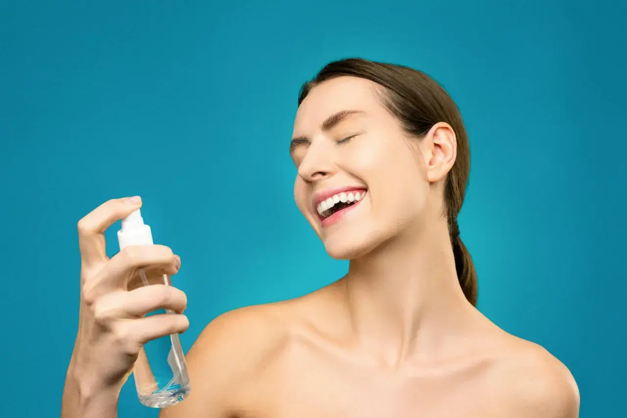 Uśmiechnięta kobieta rozpyla na twarz hydrolat. To naturalny tonik, który odświeża i nawilża skórę.