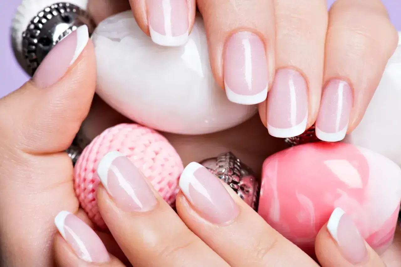 Elegancki manicure francuski na zadbanych dłoniach, otoczony różowymi i białymi ozdobami. To kwintesencja klasyki, czyli co to manicure.