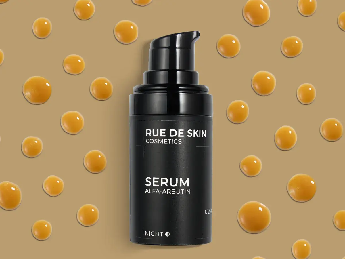 Czarny flakonik serum z alfa arbutyną, otoczony kroplami o bursztynowym kolorze, na beżowym tle.