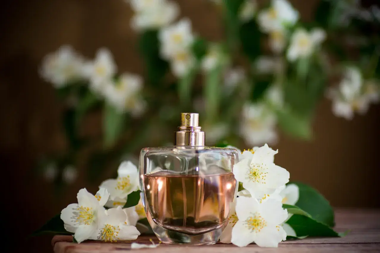 Perfumy w szklanej butelce otoczone białymi kwiatami jaśminu. Zapach jaśminu unosi się w powietrzu, tworząc romantyczną atmosferę.
