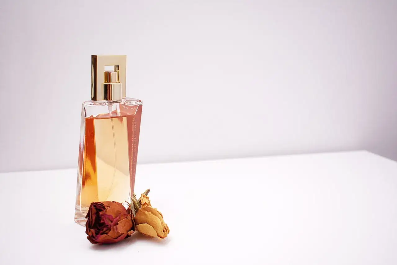 Elegancka butelka perfum z płynem w kolorze bursztynu, ozdobiona złotą nakrętką. Obok leżą dwie zasuszone róże, sugerujące subtelny zapach piżma.