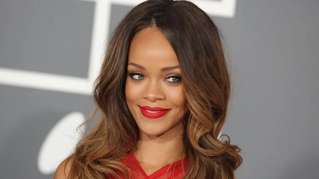 Rihanna z burzą brązowych loków, które sprytnie pomagają jak ukryć wysokie czoło. Czerwone usta i zielone oczy.