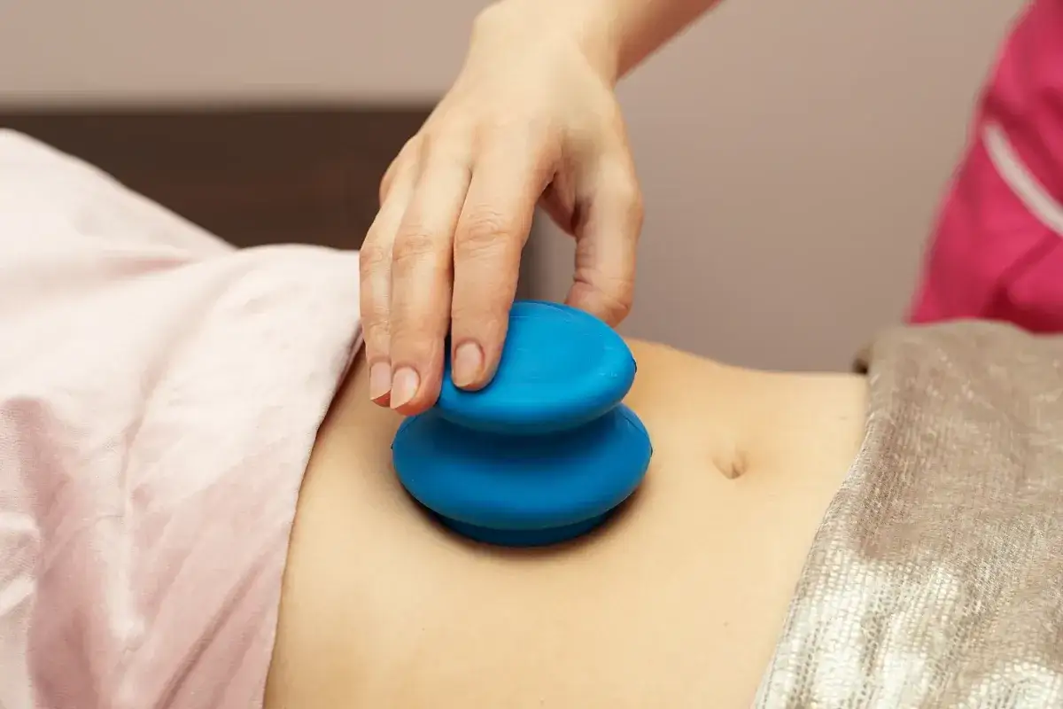 Dłoń terapeuty wykonuje masaż bańką chińską na brzuchu. Choć zabieg ma wiele zalet, warto znać potencjalne masaż bańką chińską efekty uboczne.