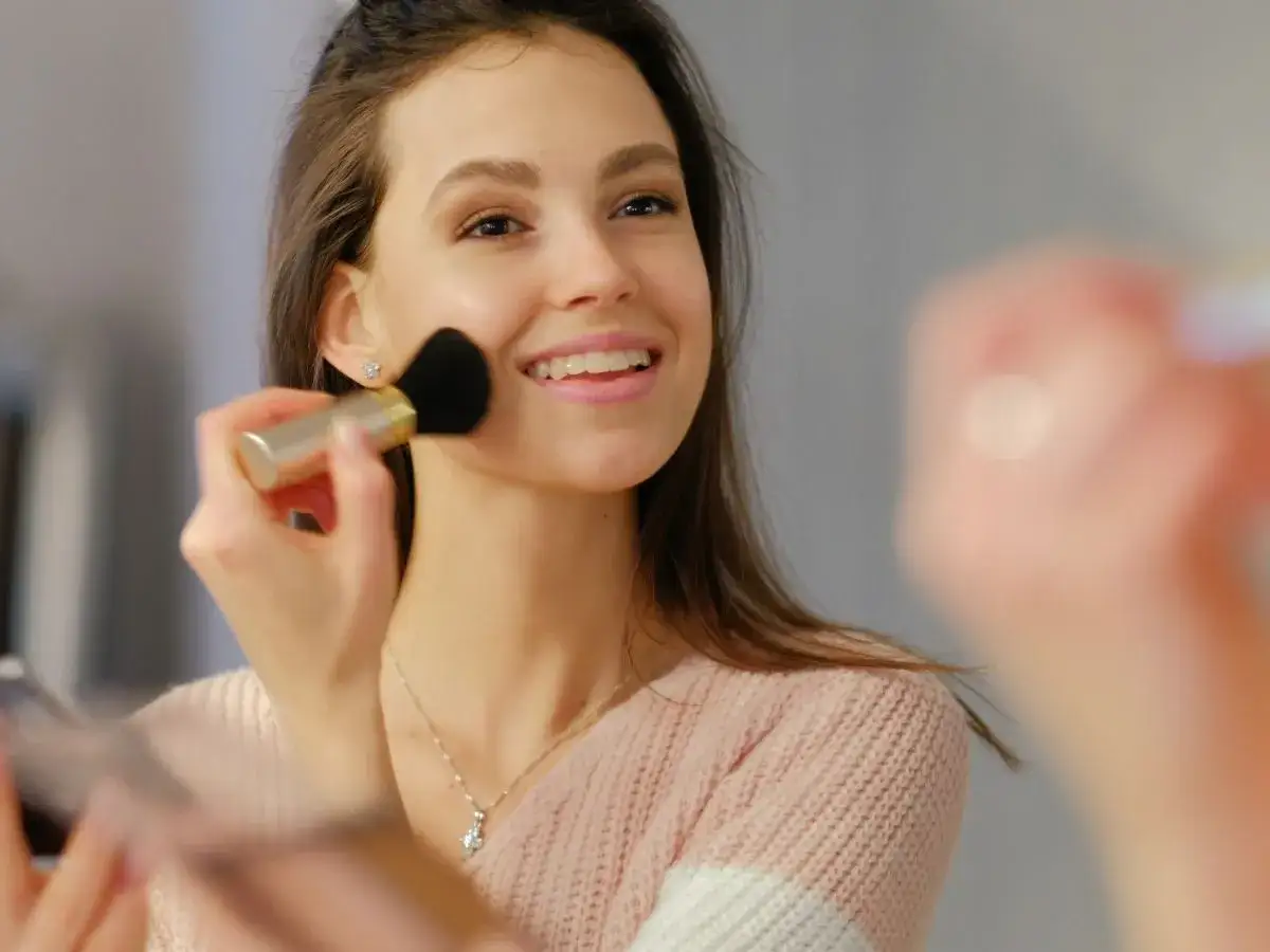 Uśmiechnięta, clean girl nakłada róż pędzlem. Delikatny makijaż podkreśla jej naturalne piękno.