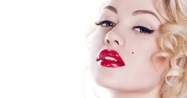 Kobieta z burzą blond loków i charakterystycznym pieprzykiem, usta w stylu Marilyn Monroe, błyszczące czerwone.